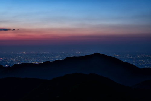大山のシルエットと眼下に広がる街の夜景、夕焼けのグラデーション