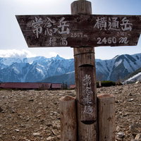 常念乗越の看板と山小屋から望む雪の山峰連峰の写真