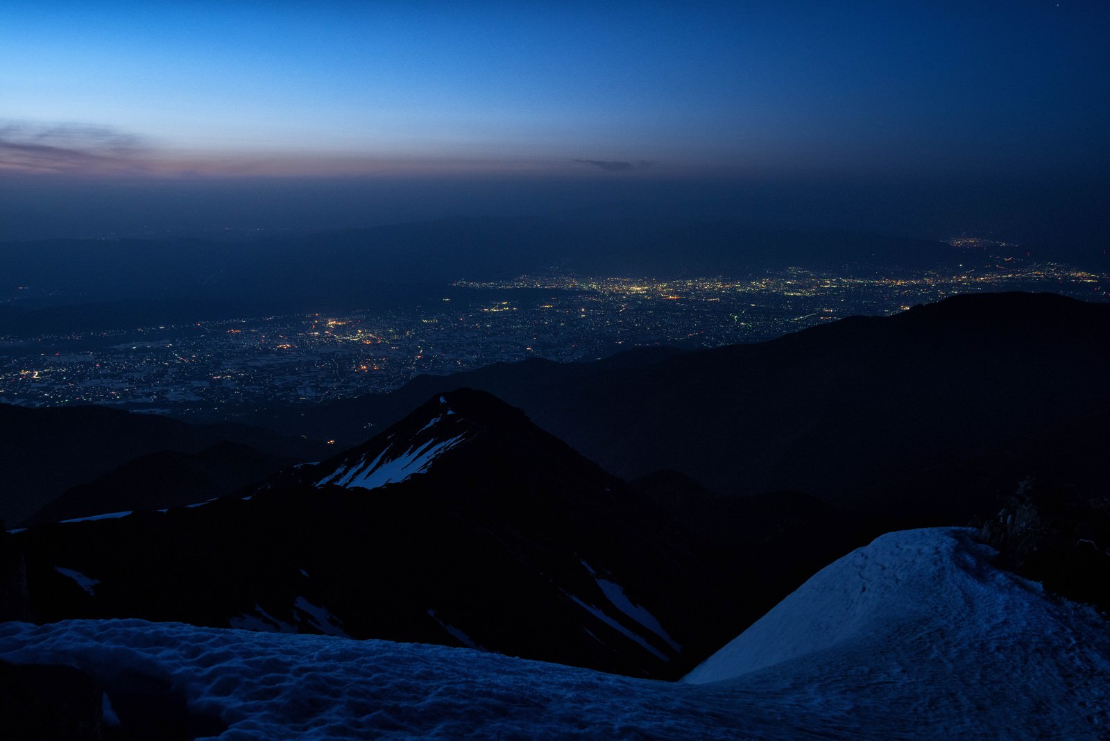 常念岳から見下ろした松本市の夜景が暮れなずむ空の下に広がる