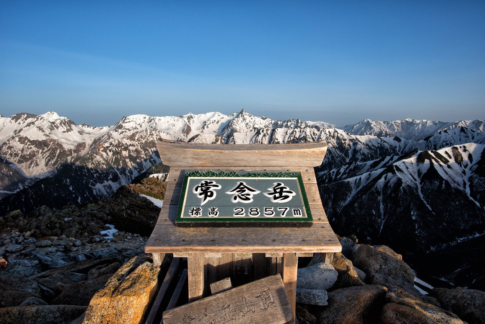 常念岳山頂の案内標識と遠方に広がる雪山の風景