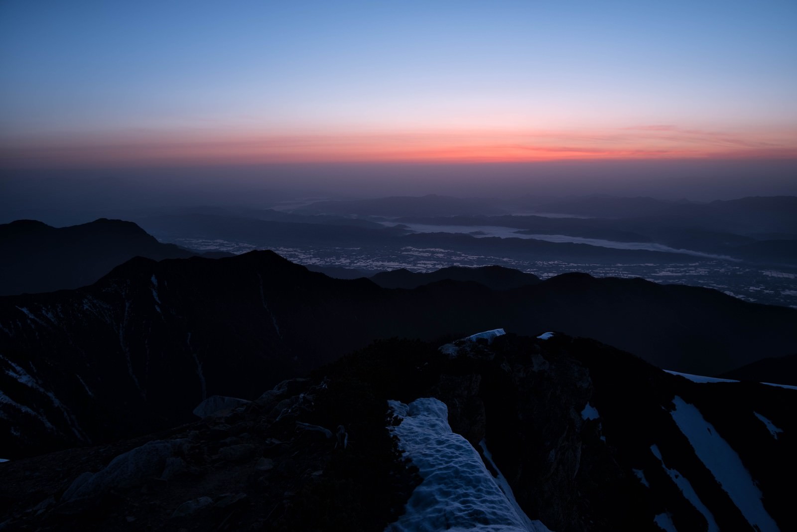薄明の空に浮かぶ常念山脈のシルエットと眼下に広がる街並みの灯り
