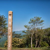 青空の下に立つ鍋割山山頂の木製標識と山並みの風景の写真