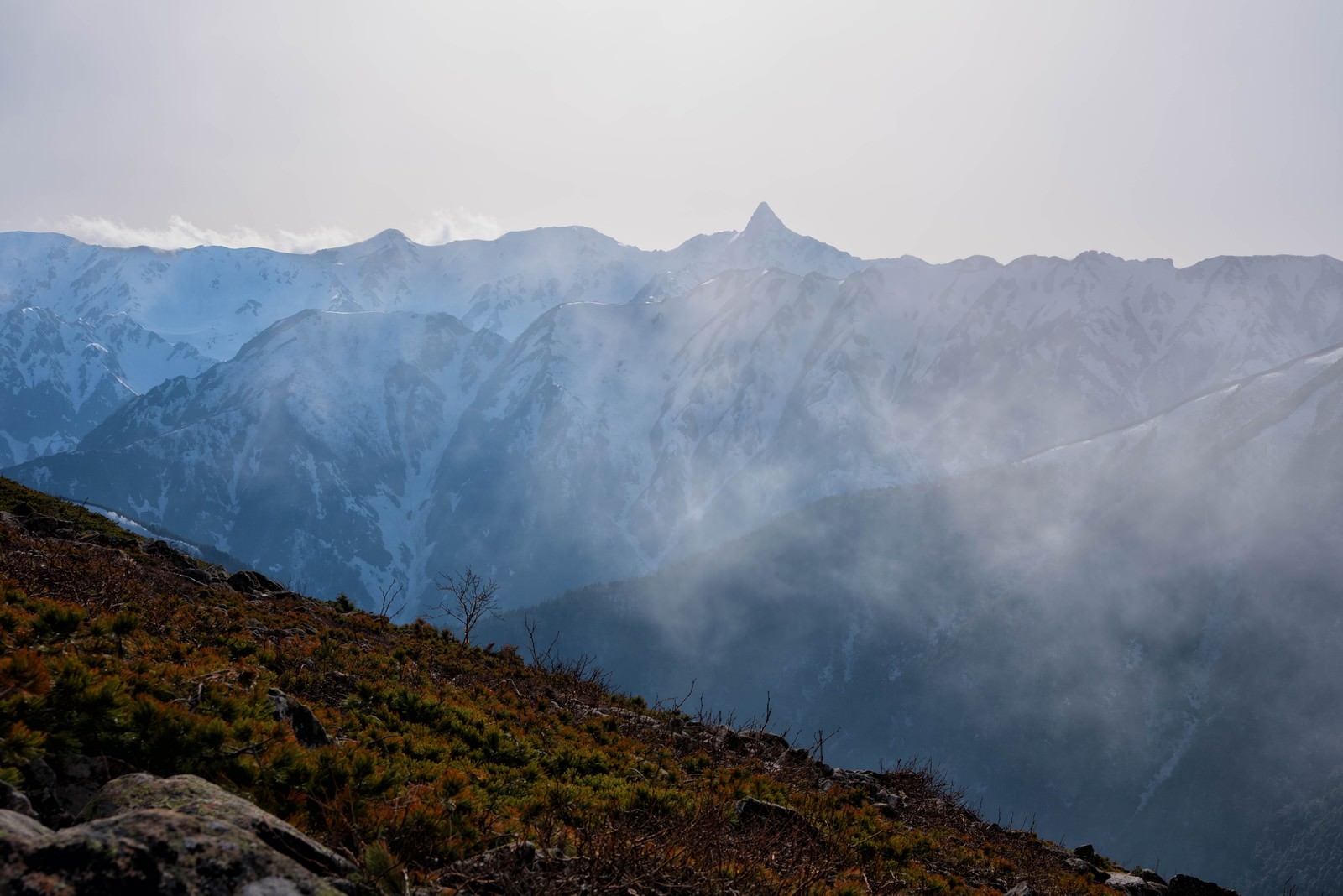 雲海に包まれた山々の中で槍ヶ岳の尖った山頂が雲の合間から見える風景