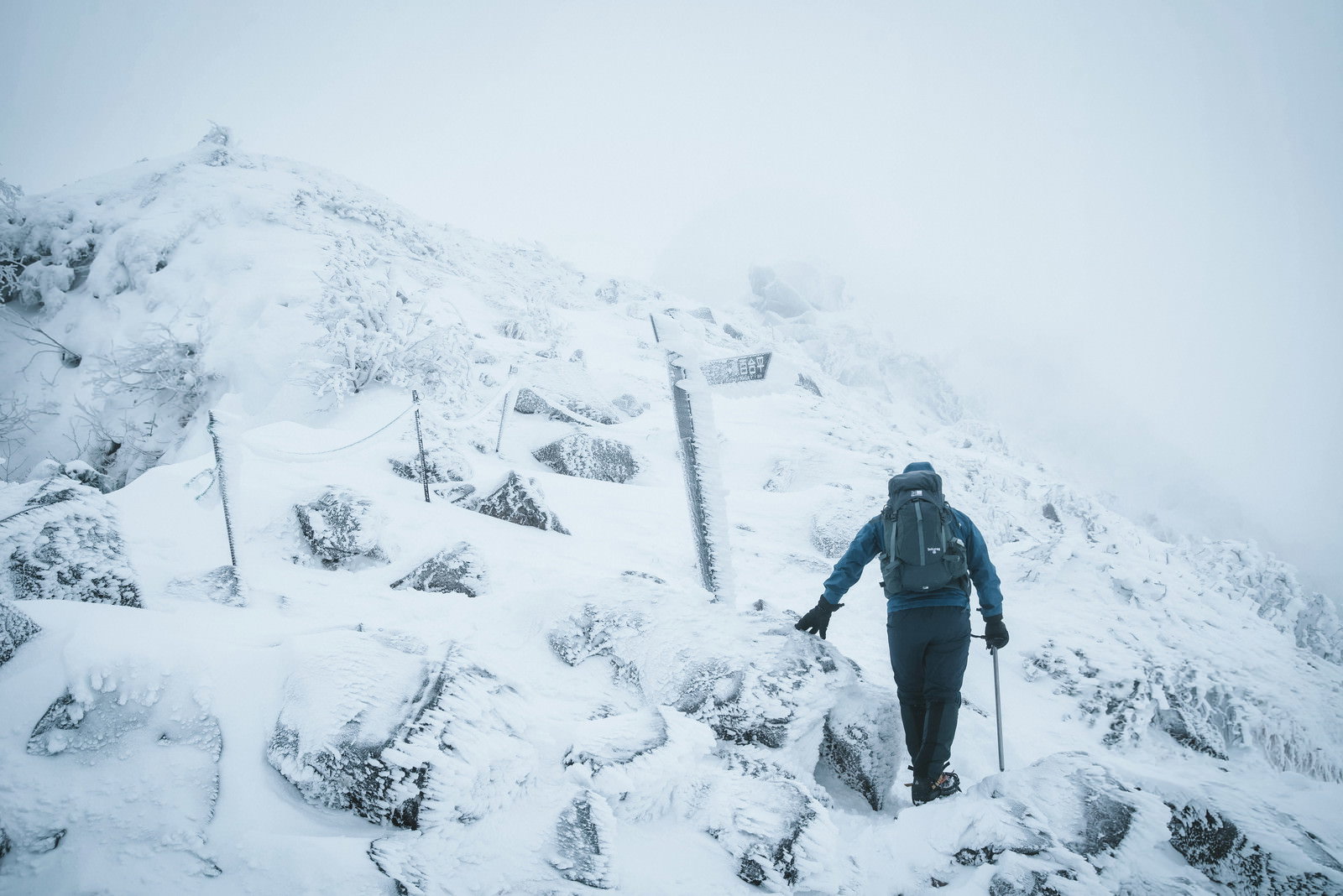 雪に覆われた山の斜面を登る登山者と樹氷が写る冬の風景