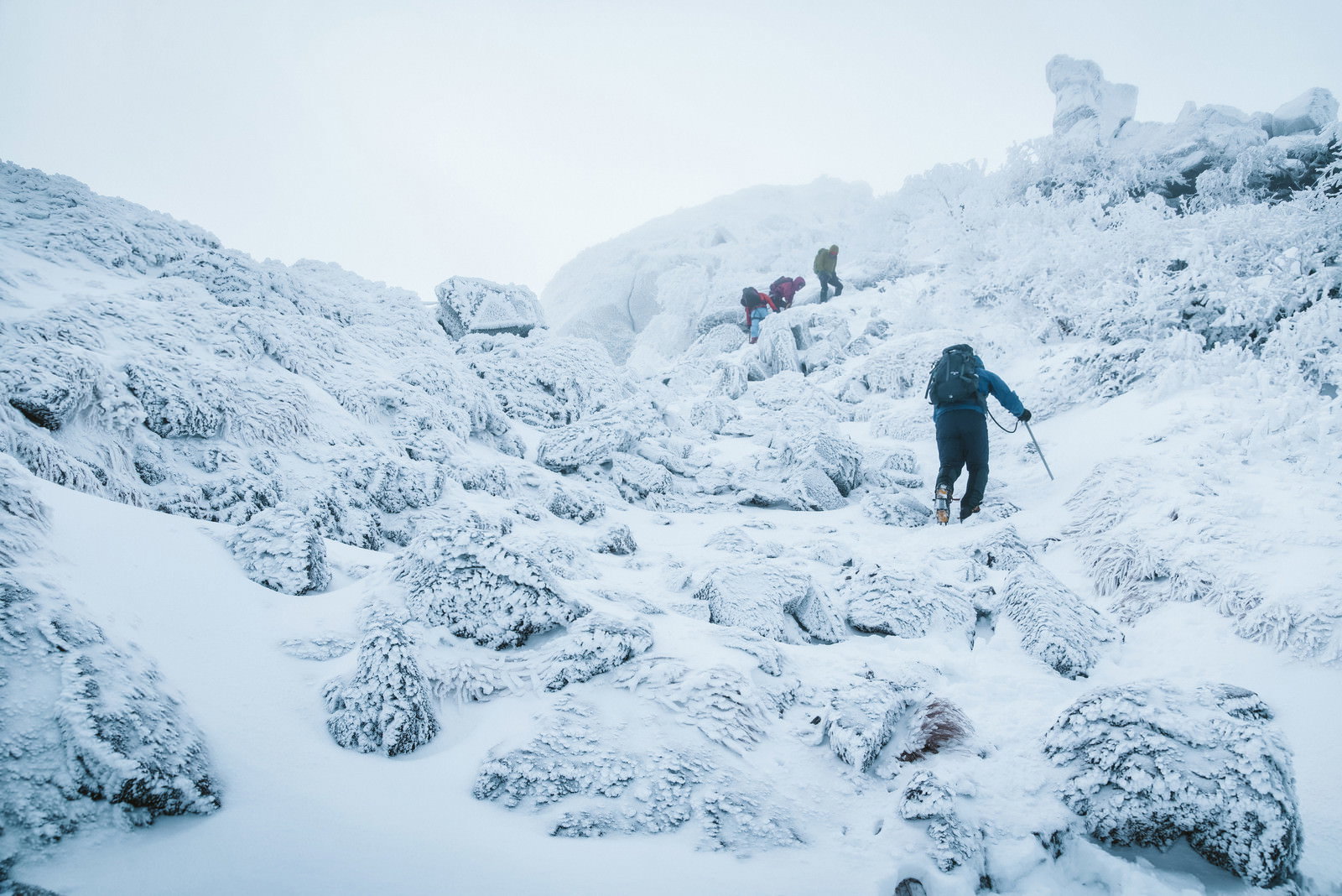 吹雪の中、雪に覆われた急斜面を歩く登山者のシルエット
