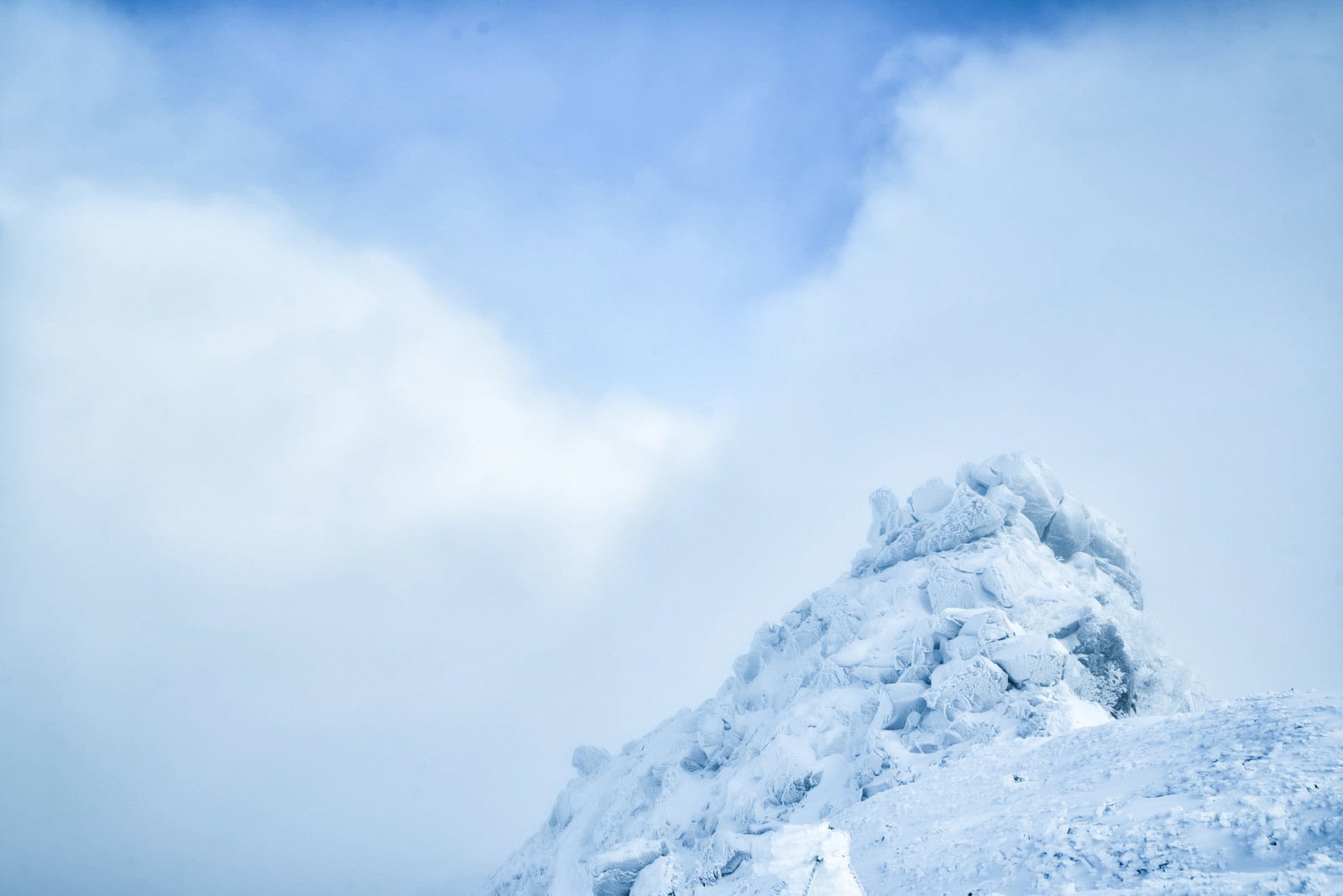 青空と白い雲の下に雪で覆われた険しい岩峰がそびえる冬山の風景