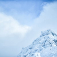 雲の切れ間から見える積雪した岩峰の冬山風景の写真