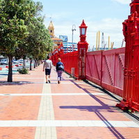 オークランド港の赤いフェンスが続く遊歩道を歩くカップルの写真