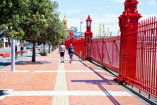 オークランド港の赤いフェンスが続く遊歩道を歩くカップル