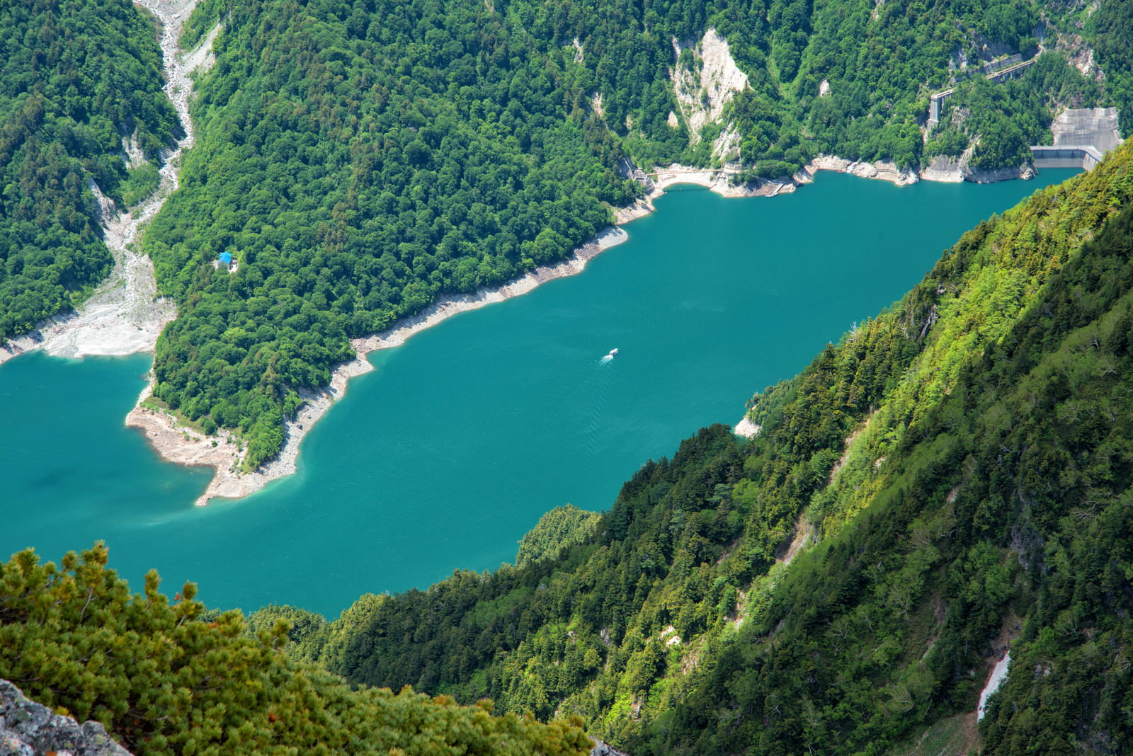 針ノ木岳から見下ろすエメラルドグリーンの黒部ダム湖と白い遊覧船