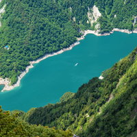 針ノ木岳から見下ろす黒部ダムと白い遊覧船の写真