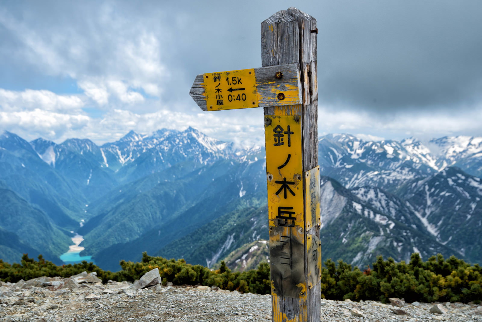 針ノ木岳山頂に立つ黄色い木製の山頂標と雪山の風景