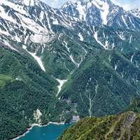 新緑期の黒部ダムと残雪の剱岳、北アルプスの山脈の写真