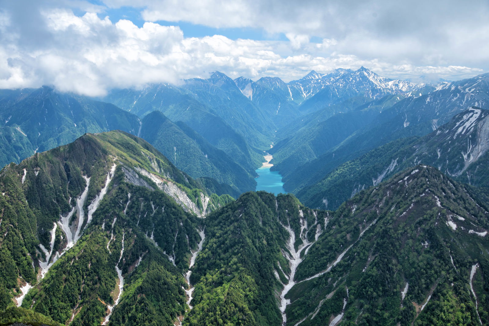 残雪が残る北アルプスの険しい山並みと新緑の風景