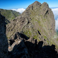 絶壁の岩場を登る登山者と雲海に青空が広がる山岳風景の写真