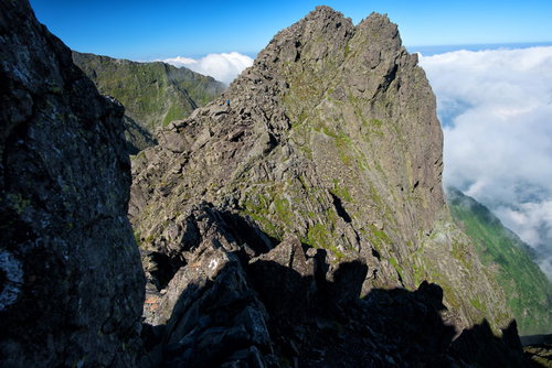 絶壁の岩場を登る登山者と雲海に青空が広がる山岳風景