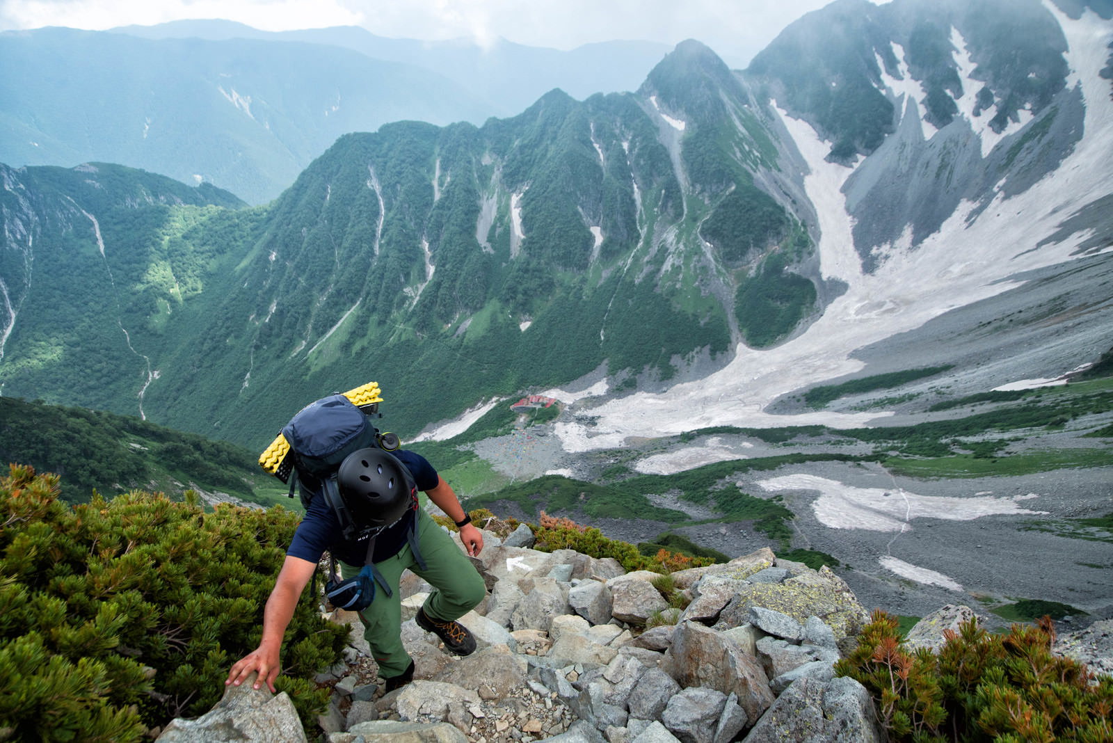 北穂高岳南陵の険しい岩場を黄色いザックで登る登山者と背景の山々