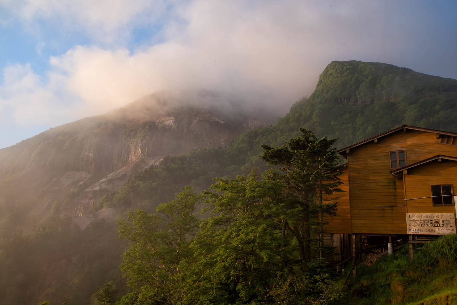 雲に包まれた硫黄岳の山腹に建つ山小屋と本沢温泉の風景