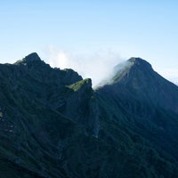 青空に連なる八ヶ岳の横岳と赤岳の尾根を歩く登山者の写真