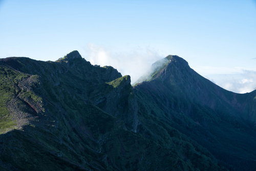 青空に連なる八ヶ岳の横岳と赤岳の尾根を歩く登山者