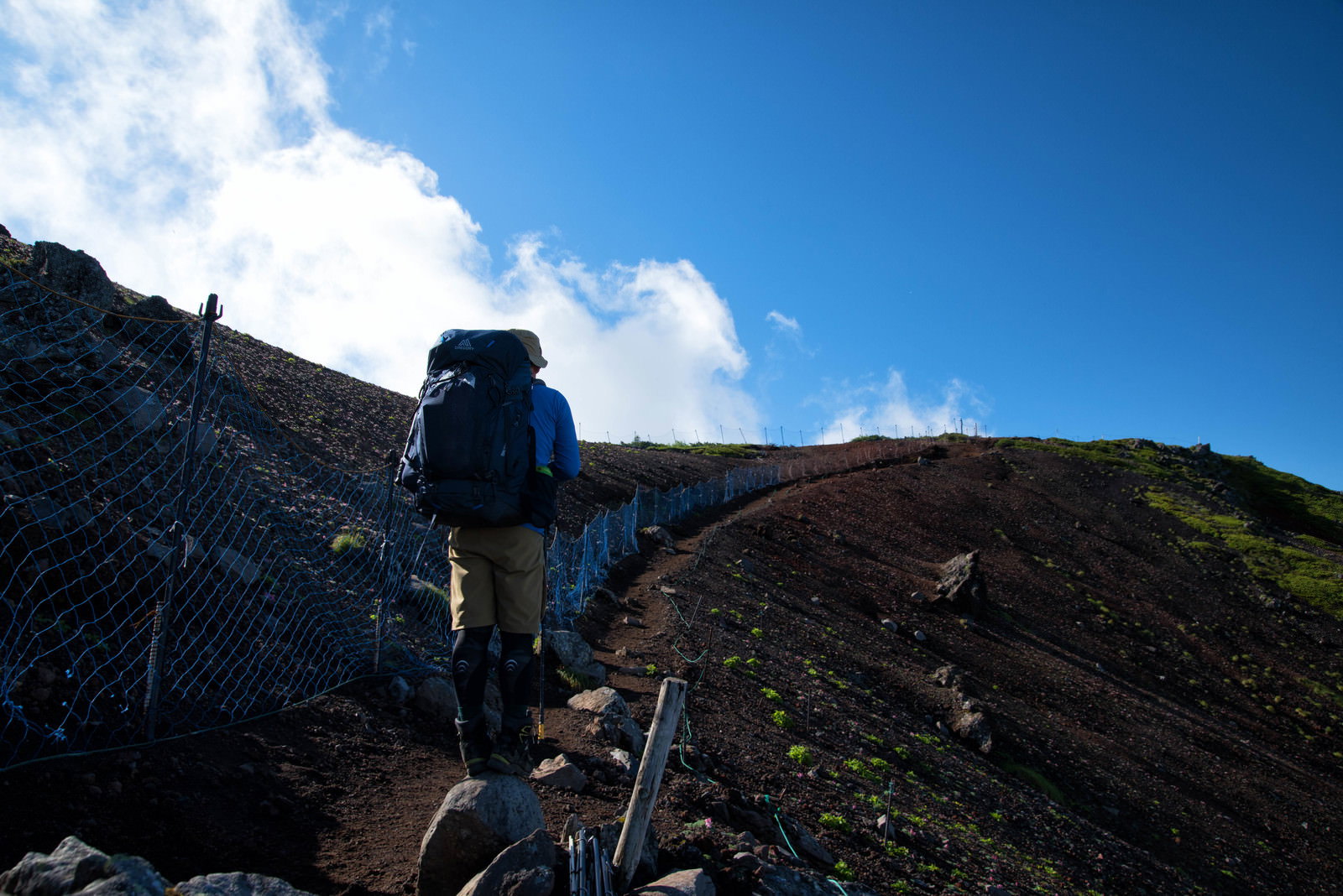 八ヶ岳の横岳登山道で保護柵の横を歩く登山者の後ろ姿
