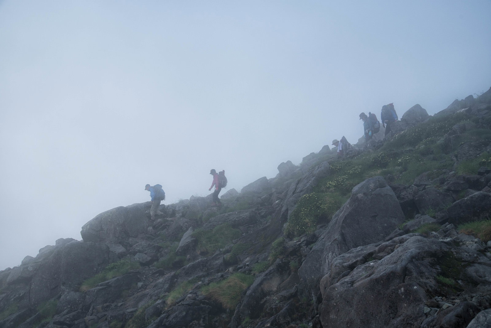 濃い霧に包まれた山中を慎重に歩く登山者