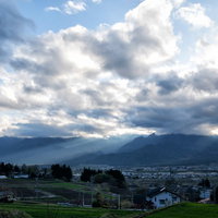 北アルプスの山並みにかかる夕暮れの光芒と住宅地の風景の写真