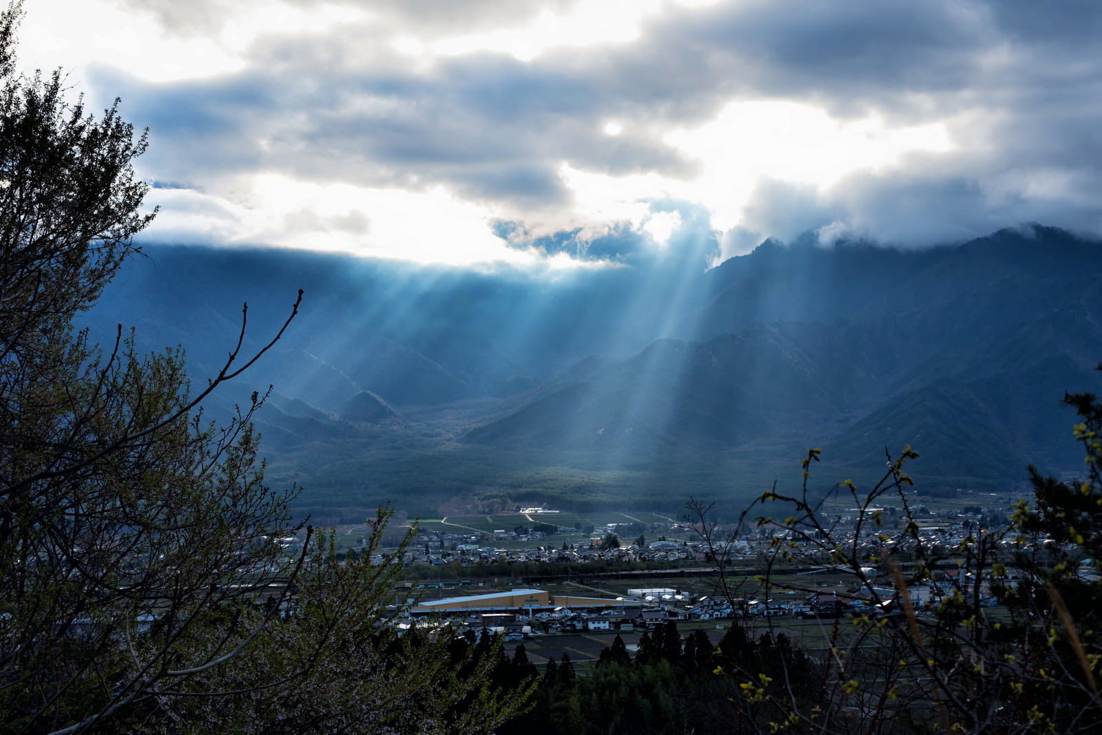 雲間から差し込む光芒が安曇野市の街並みを照らす風景