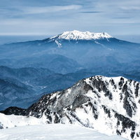 薄雲から頭を出す御嶽山と木曽前岳の雪山景観の写真