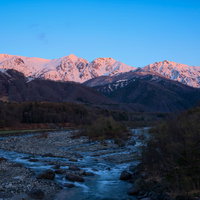 朝焼けに染まる白馬三山と霧の渓流の写真