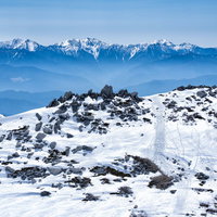 雪残る中岳のガレ場と南アルプスの山々の写真