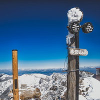 冬の赤岳山頂に立つ赤茶色の木製指導標と雪景色の写真