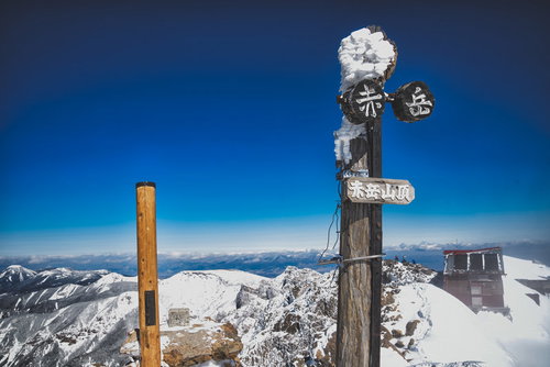 冬の赤岳山頂に立つ赤茶色の木製指導標と雪景色