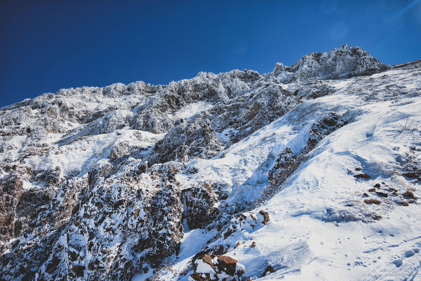 青空の下、雪に覆われた険しい岩壁が立ちはだかる冬山の風景