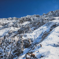 厳冬期の雪山に立ちはだかる岩壁と氷結した岩場の写真