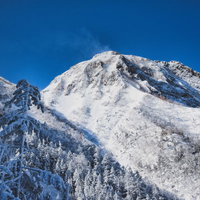 青空に雪煙が舞い上がる阿弥陀岳（八ヶ岳連峰）の写真