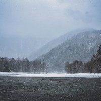 吹雪く梓川と雪化粧の山々（上高地）の写真