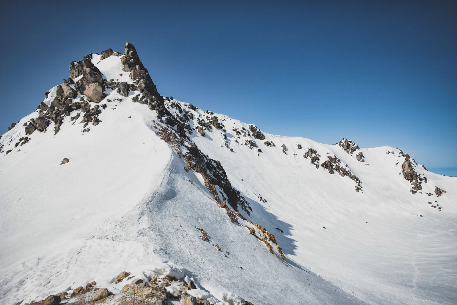 青空の下、雪に覆われた焼岳南峰の山頂部分