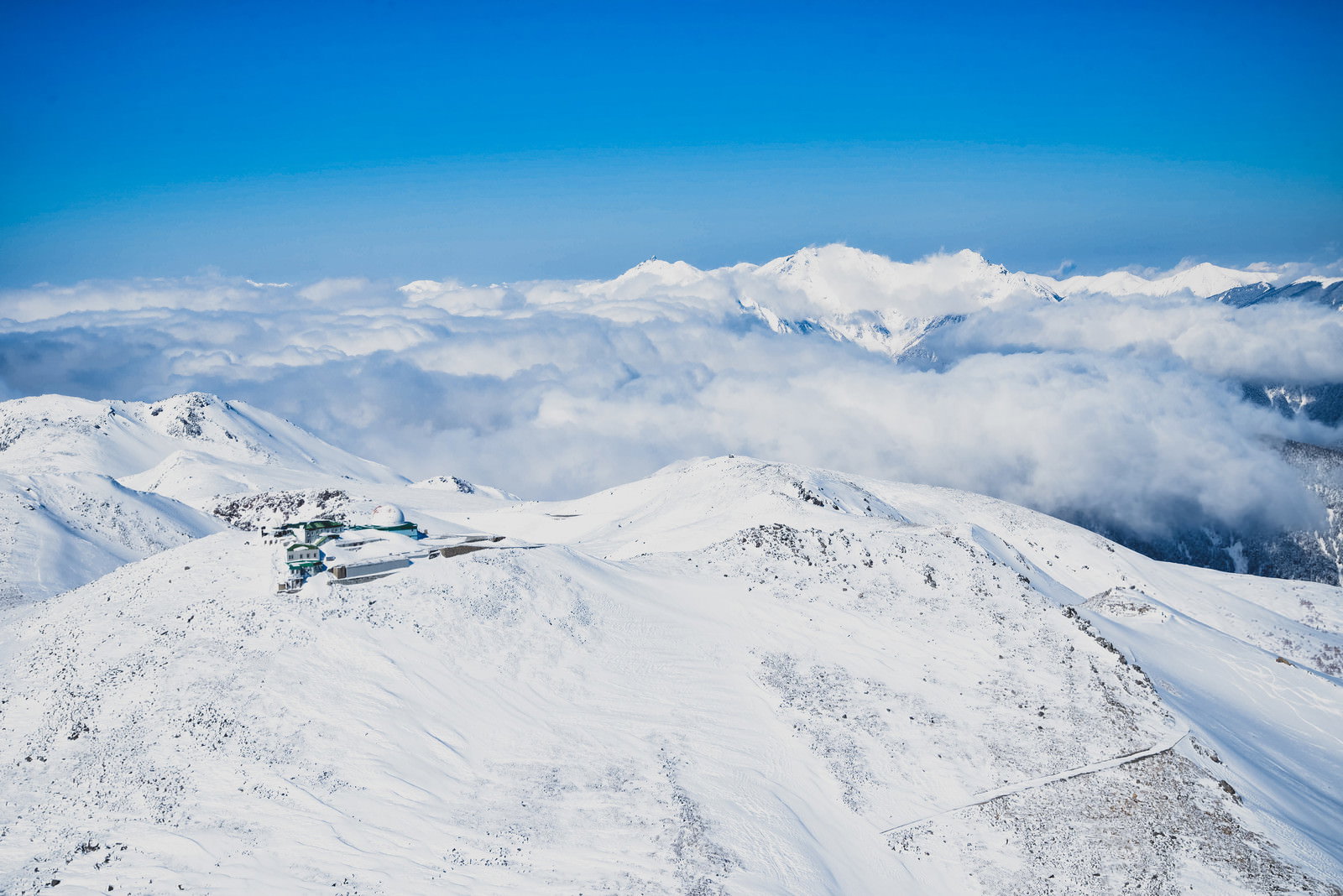 雪化粧した穂高連峰の山々と白いコロナ観測所が青空の下に広がる冬の風景