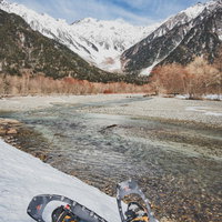 上高地から流れる川沿いでスノーシューを装着し雪山トレッキング中の登山者の写真