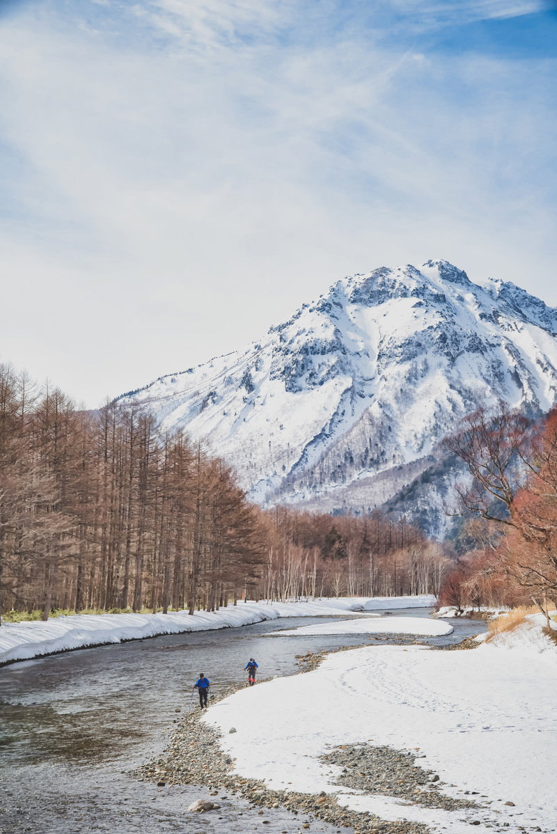雪景色の上高地で梓川沿いを歩く登山者と雪化粧した穂高連峰