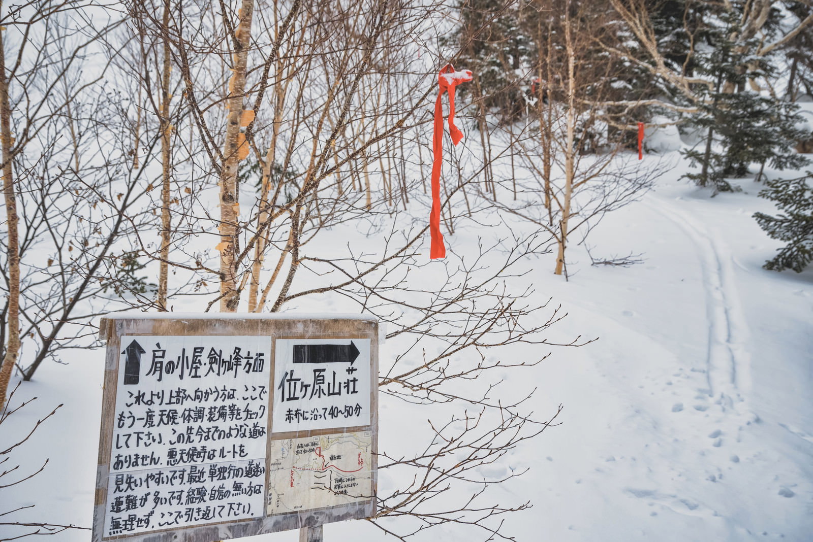 雪に覆われた乗鞍岳の登山道に立つ位ヶ原山荘への木製看板