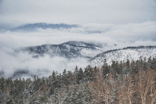 覆われた雲の中から顔を出す積雪した雪山の冬景色