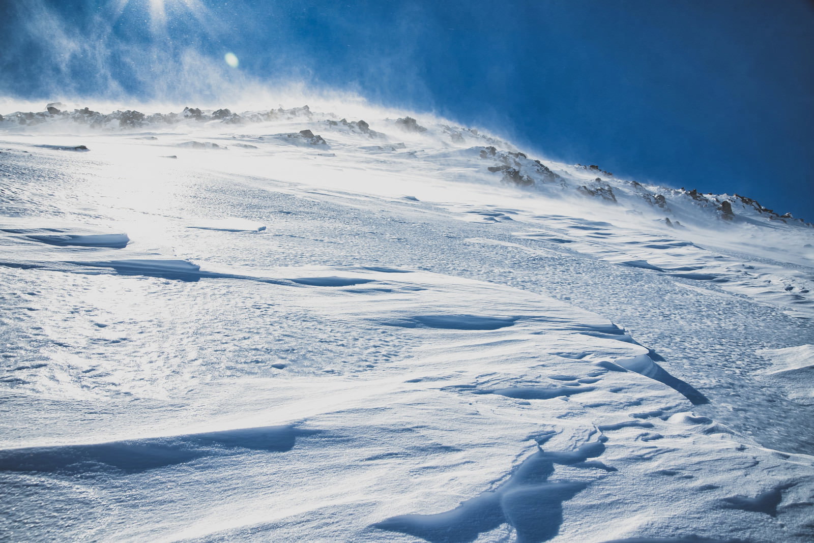 白く積もった雪の上に風で作られた波模様が広がる山の斜面