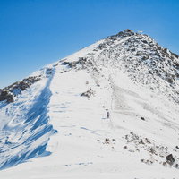 青空の下、積雪した剣ヶ峰を目指す冬山の登山者の写真