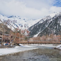 厳冬期の上高地を流れる梓川と雪化粧した木製の吊橋（河童橋）の写真