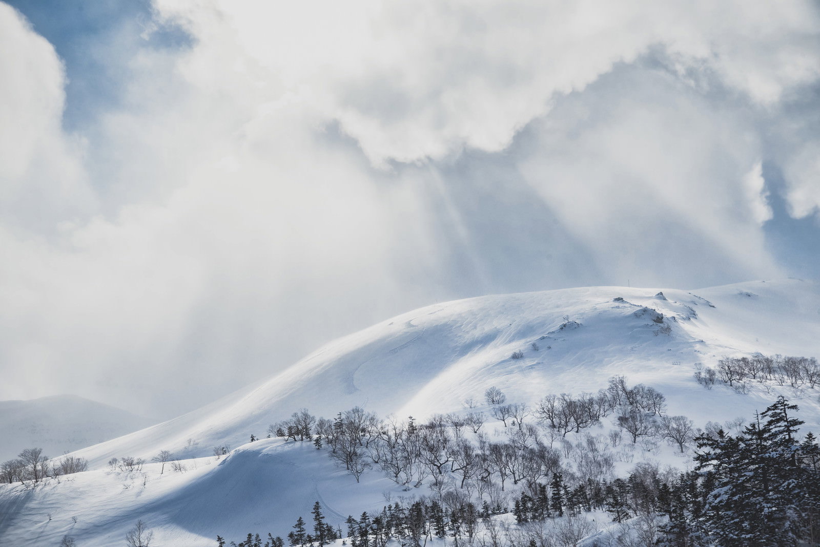 雲の隙間から光芒が差し込む雪化粧した乗鞍高原の冬景色
