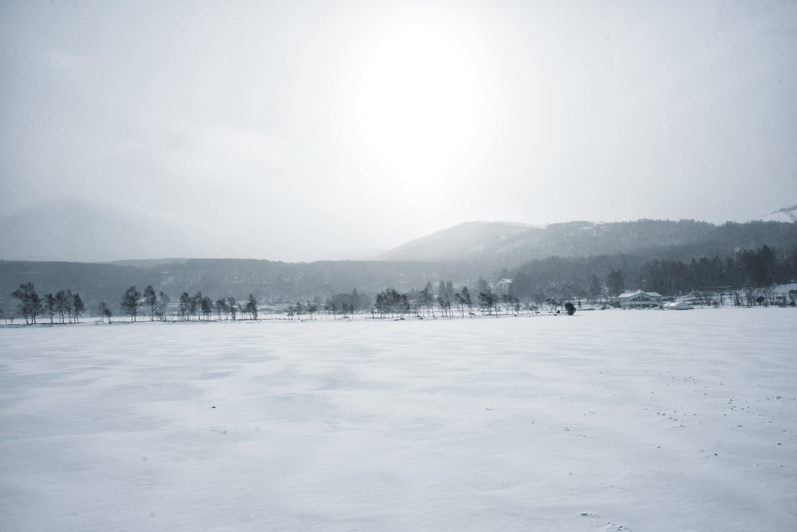 雪に覆われた凍結した白樺湖と遠くに見える雪山の冬景色