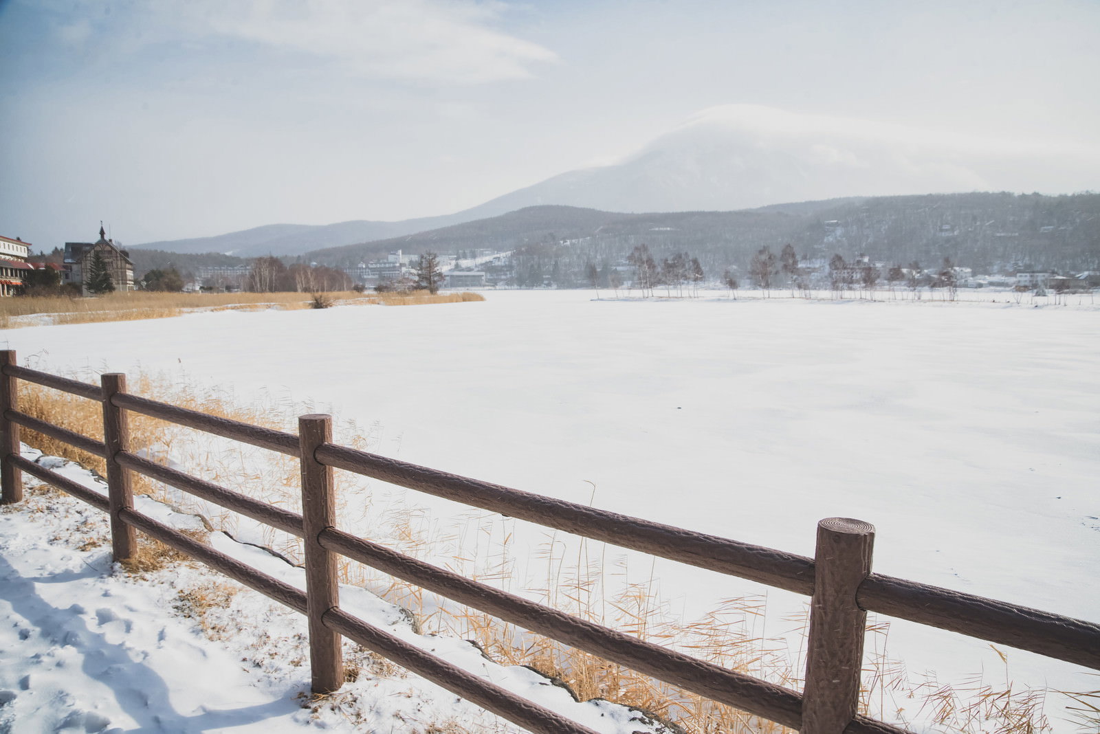 雪に覆われた白樺湖と山々を木製の柵越しに見た冬の遊歩道風景