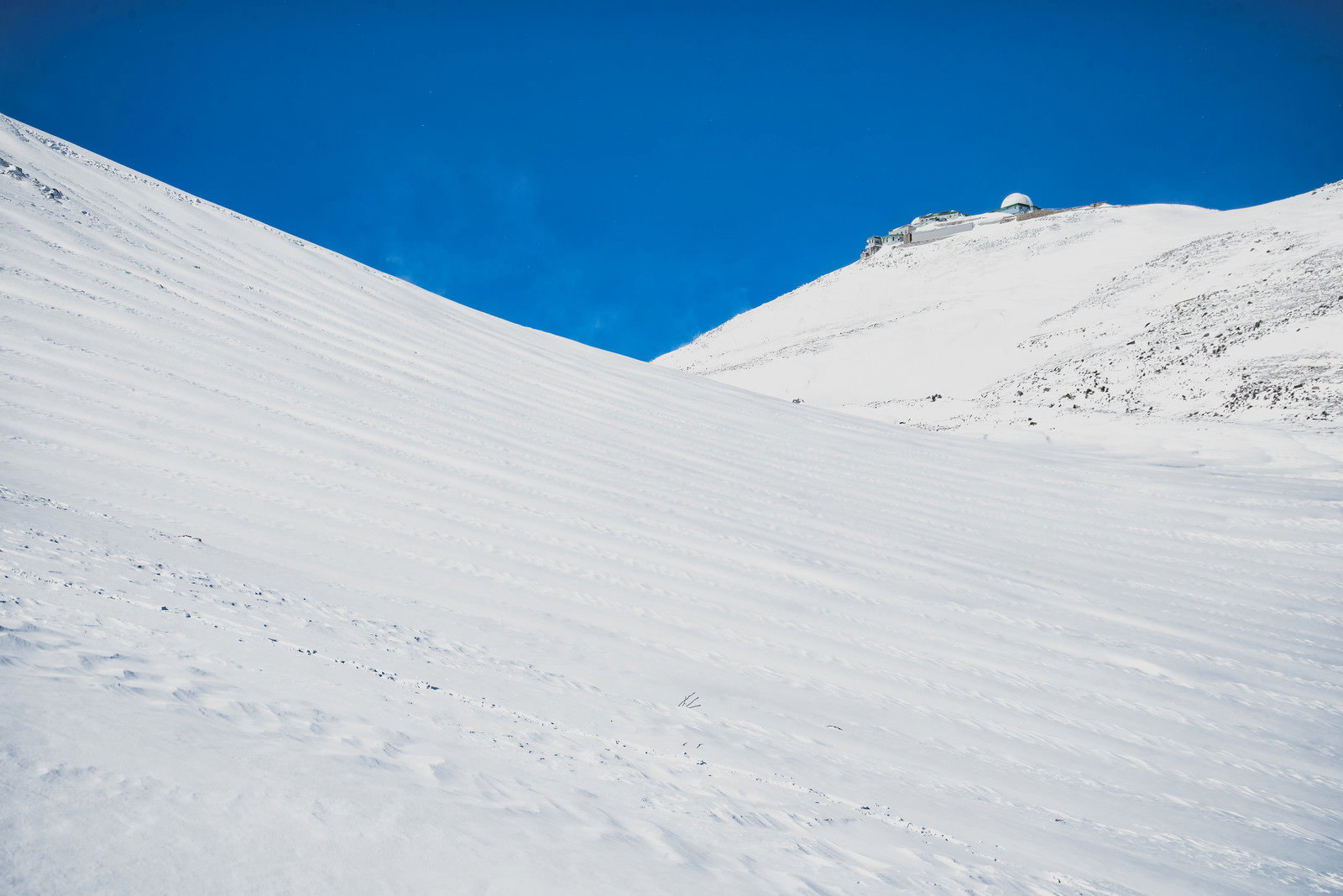 青空の下、雪に覆われた摩利支天岳山頂に設置されたコロナ観測所